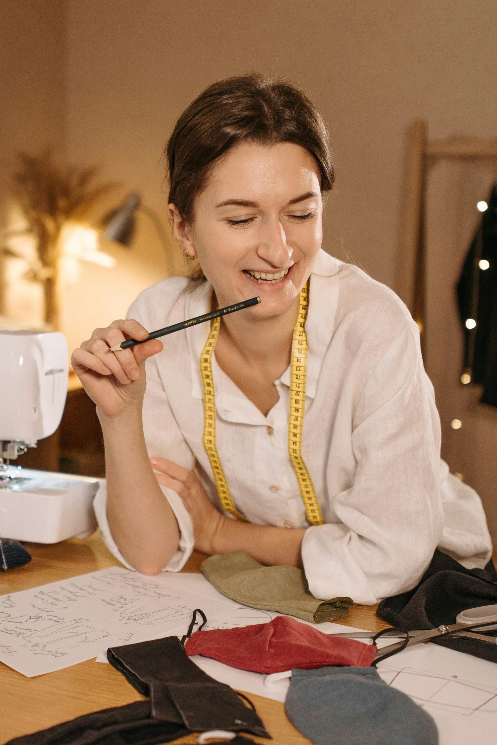 A young woman seamstress smiling while working on sewing projects in a cozy studio.